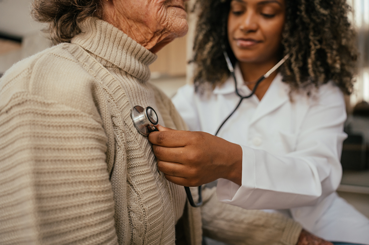 Healthcare professional listening to an elderly woman’s heart
